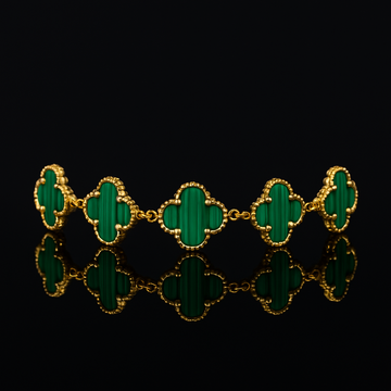 Gold bracelet with green clover-shaped stones on a black background