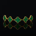 Gold bracelet with green clover-shaped stones on a black background