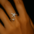 Hand wearing two star-shaped rings on a dark background