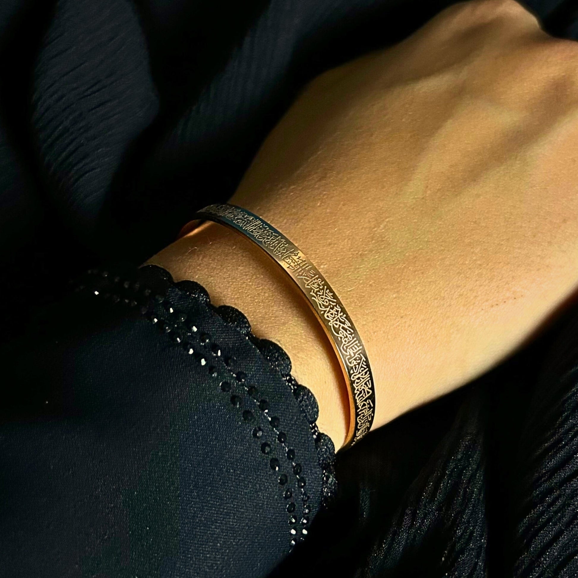 Hand wearing a gold bracelet with a dark background