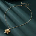 A gold-colored necklace with a floral pendant on a chain, displayed against a dark background.