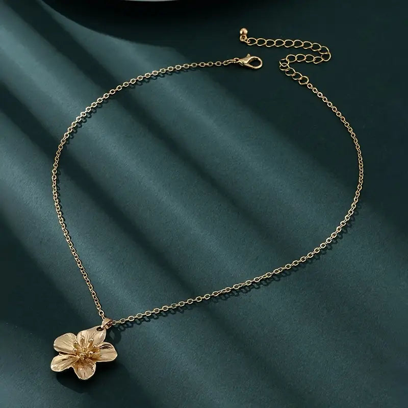 A gold-colored necklace with a floral pendant on a chain, displayed against a dark background.